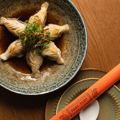 Looking down at a shallow plate of dumplings in a sauce, with chopsticks wrapped in orange paper alongside.