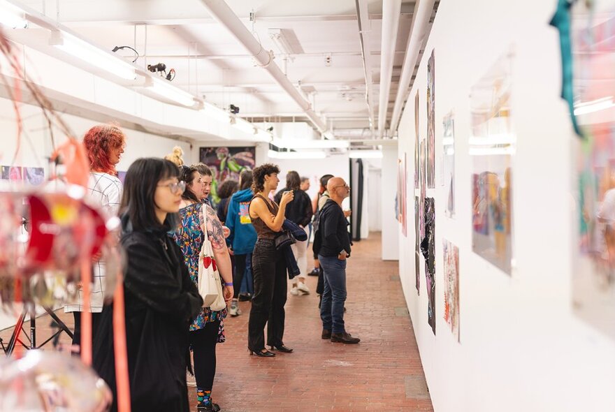 Groups of people looking at art in a long, narrow gallery space.