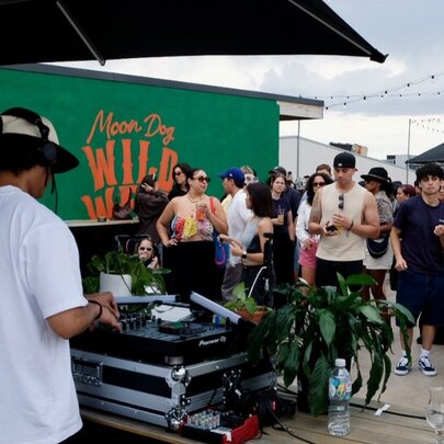 DJ at a music desk at an outdoor rooftop venue, people looking on.
