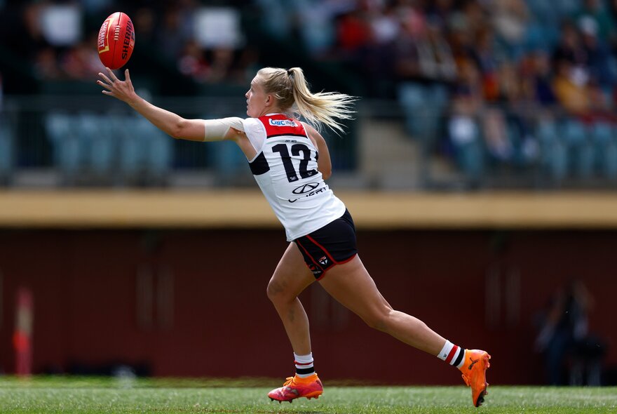 An AFLW player in a St Kilda jersey reaching to catch a red football during a game. 