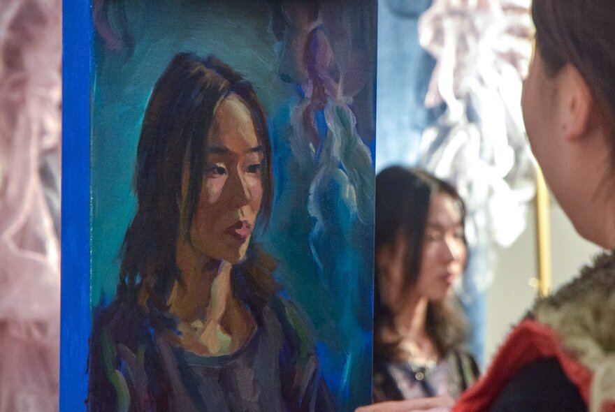 An artist painting the portrait of a woman seated in front of her.