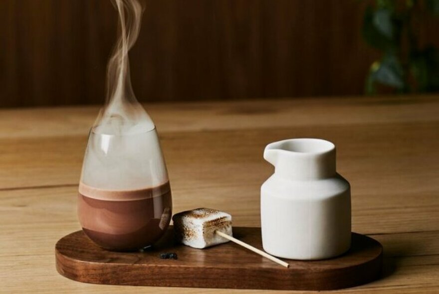 A tray with a smoking hot chocolate, marshmallow dipper and a milk jug.