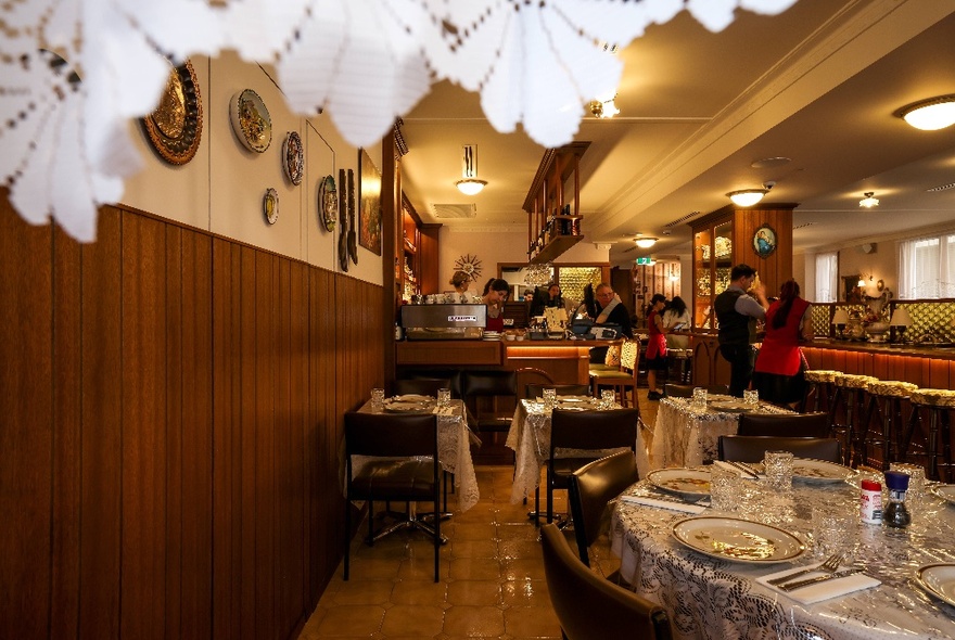 The interior of a restaurant that looks like a lounge room with kitsch artworks on the wall, chandeliers, and lace curtains.