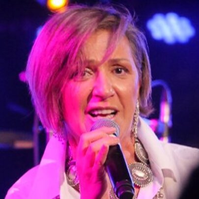 Singer, Noria Letts, singing into a microphone with a pink stage light shining on her short blonde hair.