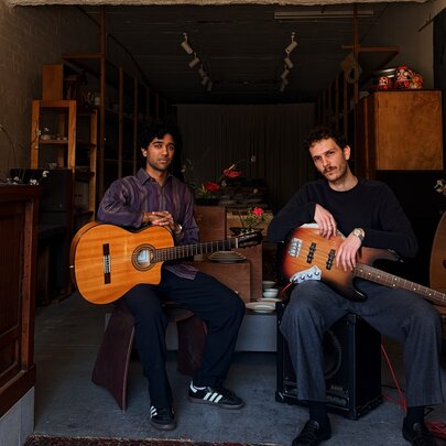 Two musicians with guitars sitting in a small gallery space.
