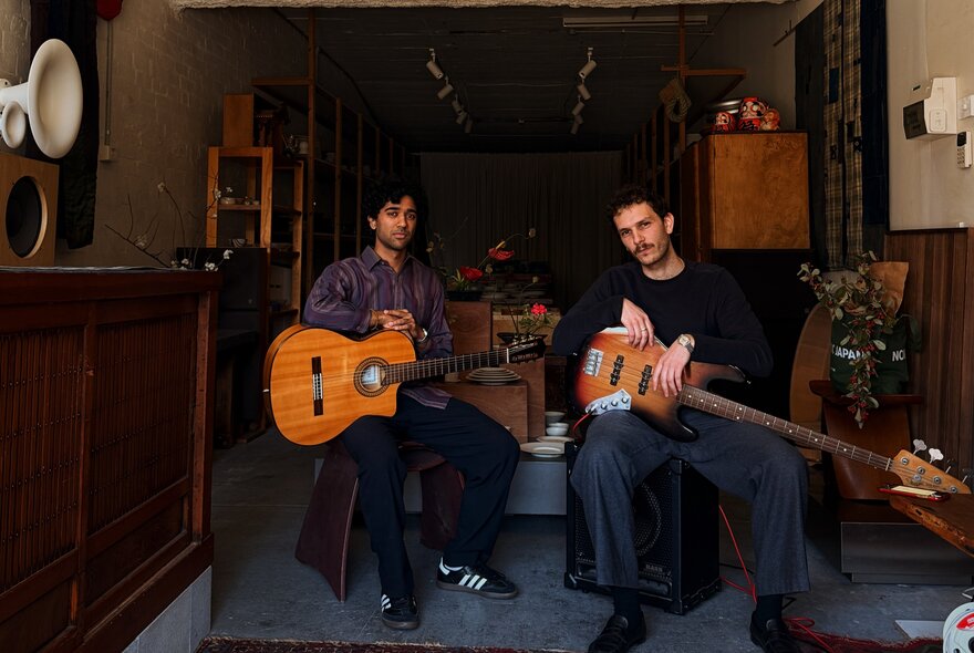 Two musicians with guitars sitting in a small gallery space.