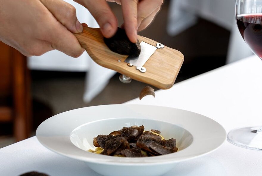 A person's hands shaving truffles into a bowl with a special shaving utensil. 