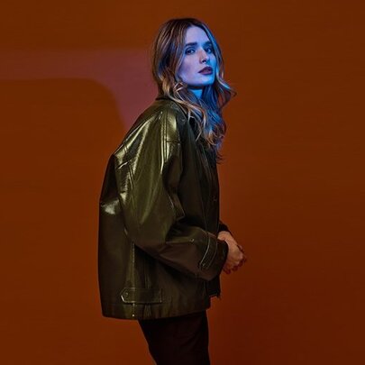 A model posing in an olive green glossy bomber style jacket.