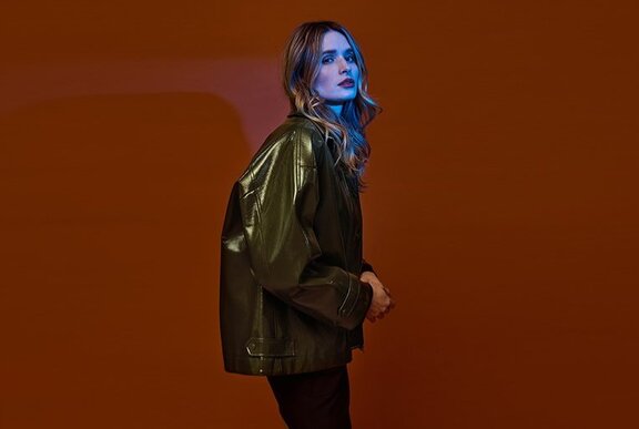 A model posing in an olive green glossy bomber style jacket.