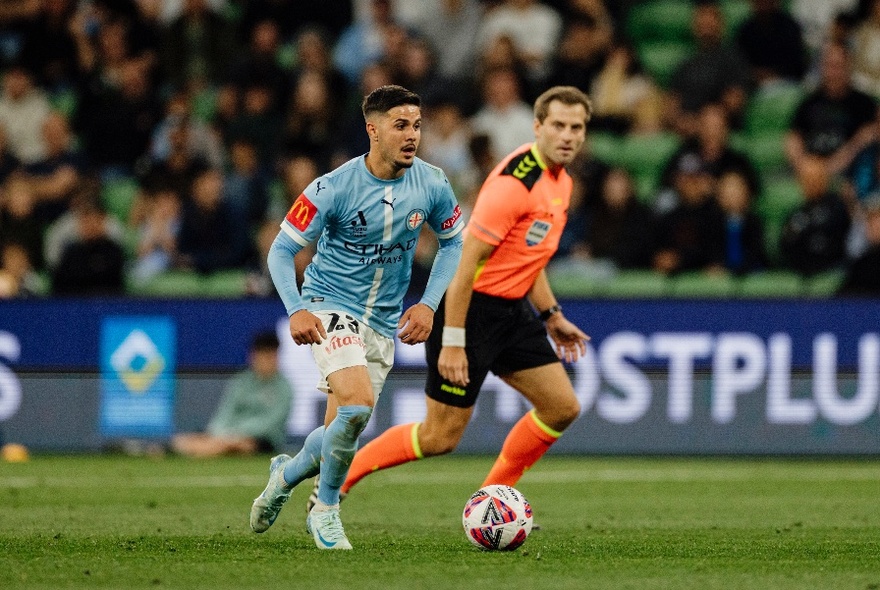 Two soccer players going for a ball in the middle of game with a blurred crowd behind. 