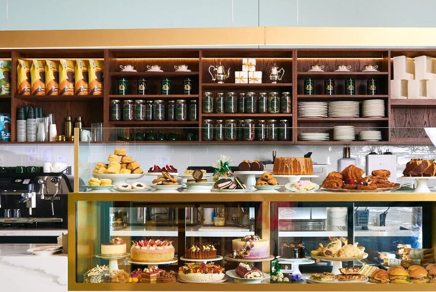 The cake display window on the counter at a bake shop, with shelves of plates and tea jars behind.