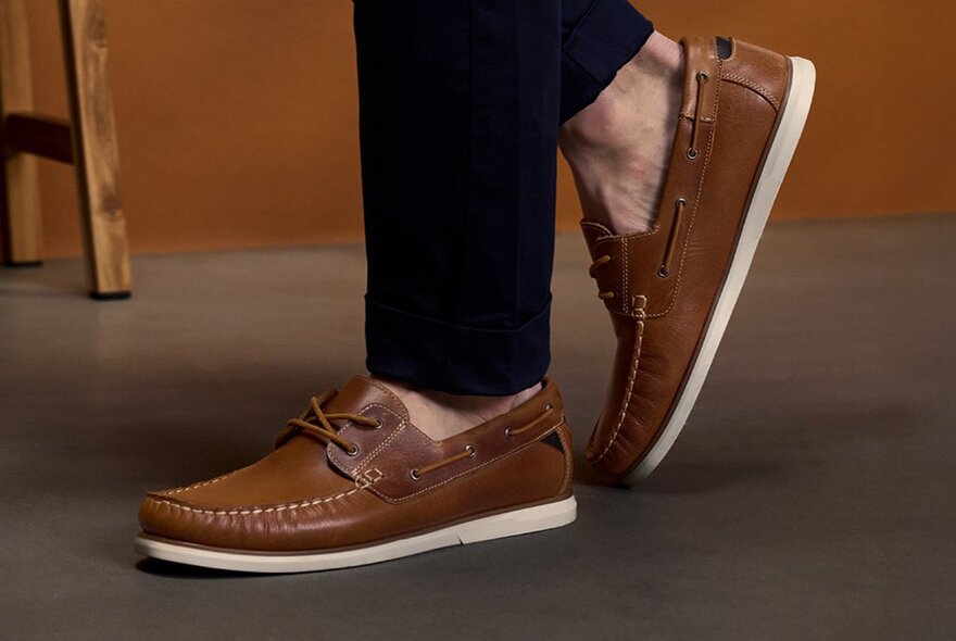 A close-up of someone's ankles and feet wearing brown boat shoes without socks.
