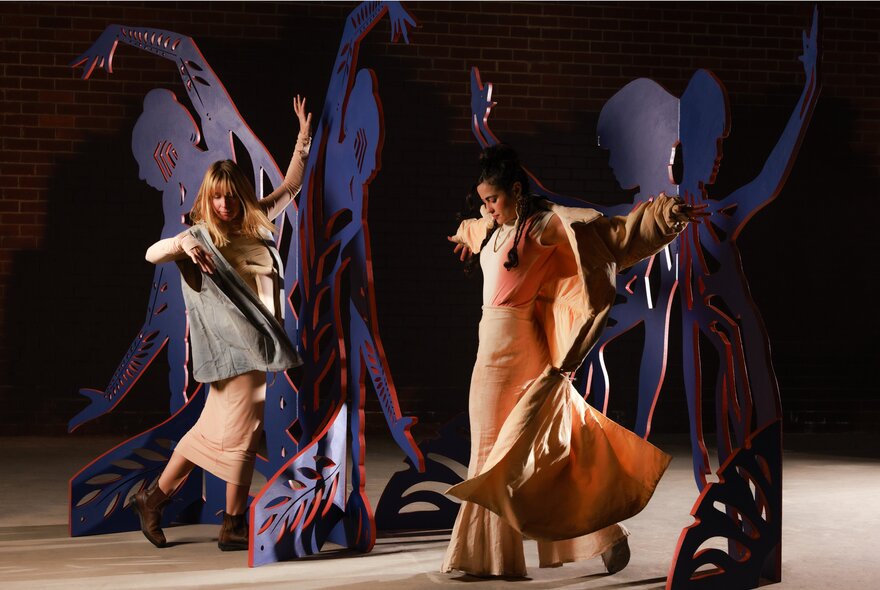 Two women dancing in a dark performance space, arms up and dresses moving.