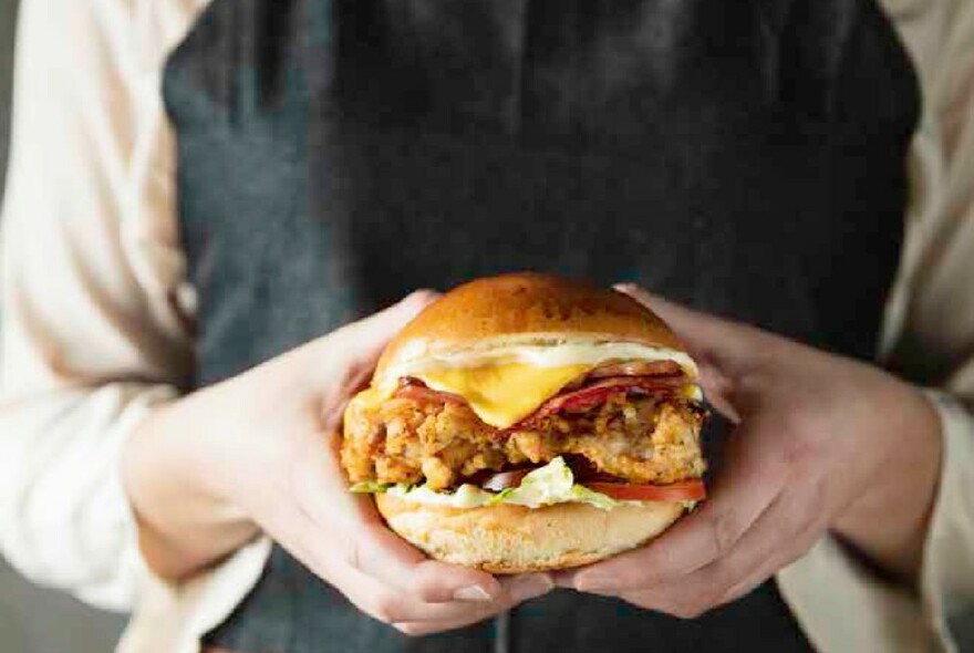 Waiter's hands holding a large burger.