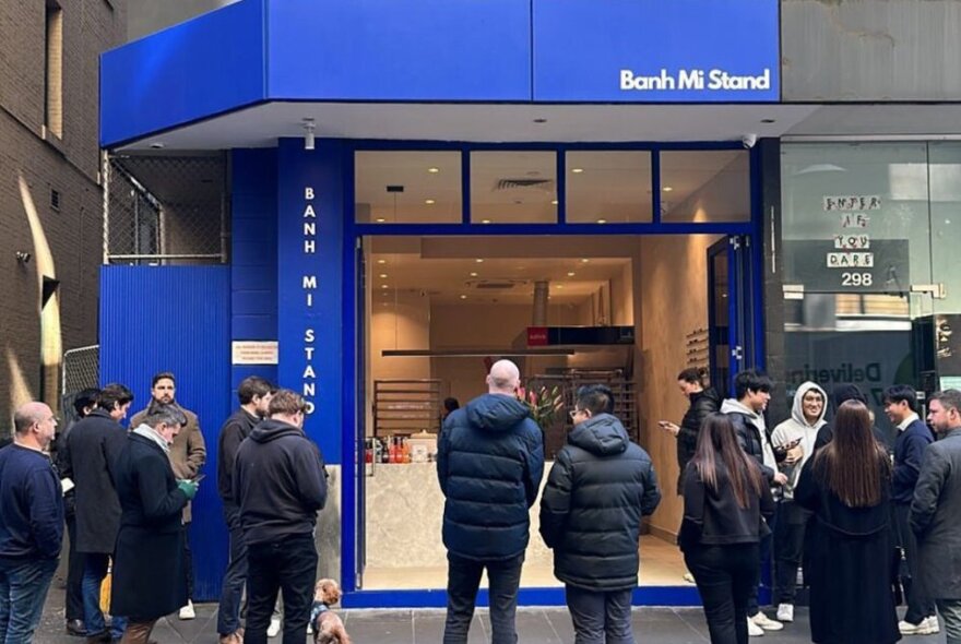 People in black coats and jackets all gathering outside a blue Banh Mi Stand store 