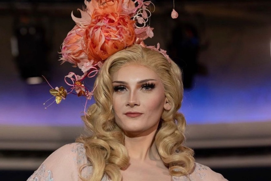 Headshot of a woman modelling a large orange floral fascinator. 