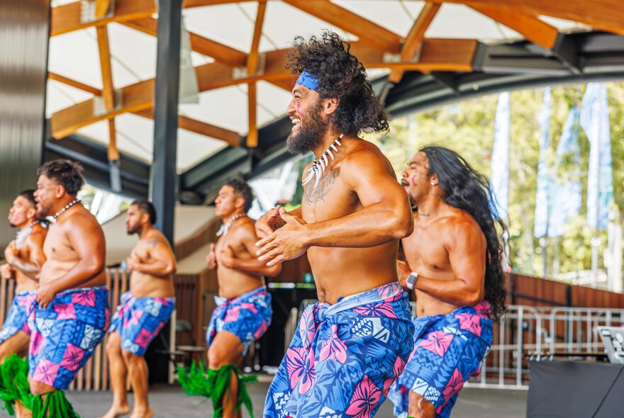 Bare-chested male Pacifka dancers wearing sarongs dancing on stage.