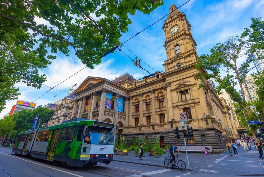 A tram going past a grand city hall building on a sunny day.