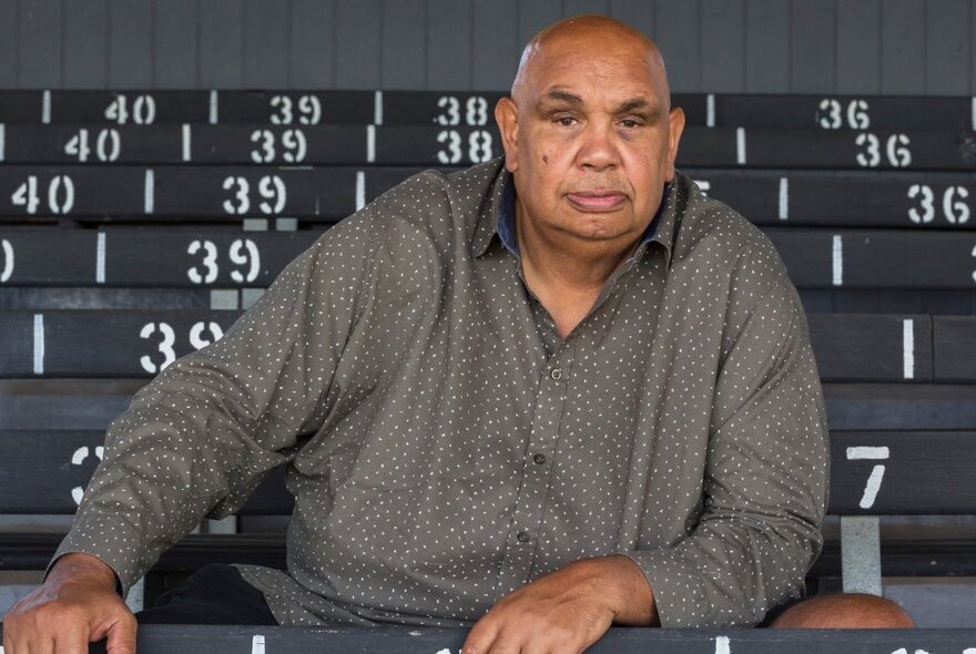 Singer-songwriter Kutcha Edwards sitting on stadium bench seating.