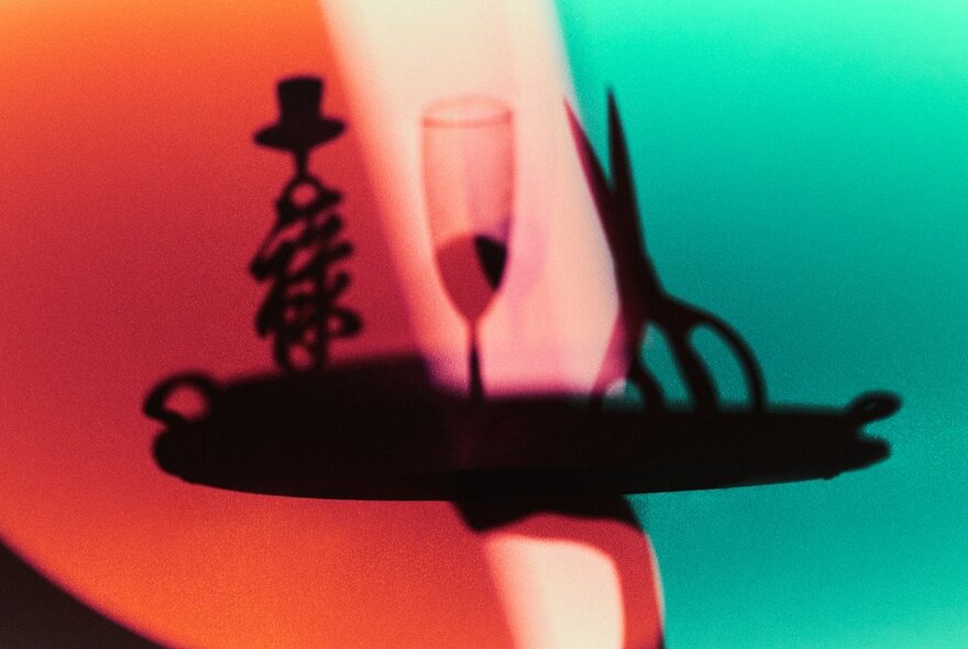 Graphic image of a candlestick, wineglass and scissors against red and green lighting.