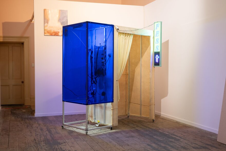 Installation artwork emulating a photo booth with blue section and curtained section.