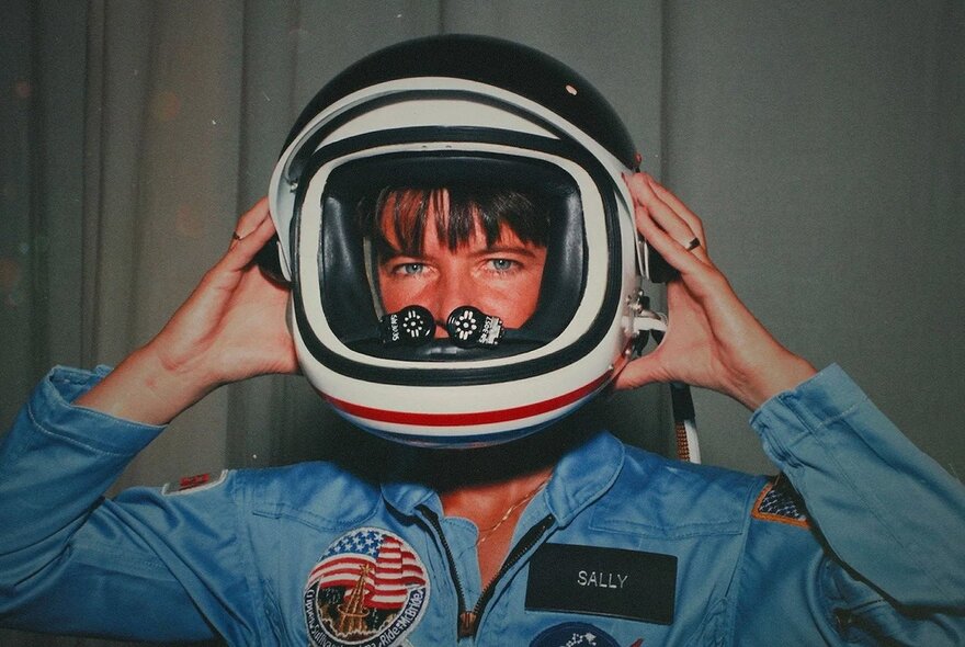 Female astronaut holding her helmet on her head.