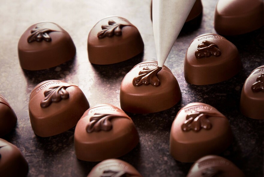 Chocolate detail being piped onto a batch of chocolates.