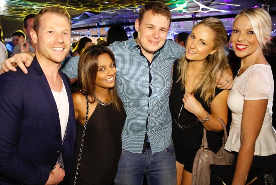 Five attractive people posing for a photo at a nightclub.