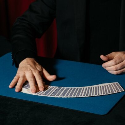 A magician's hands performing a card ribbon spread on a close-up mat.
