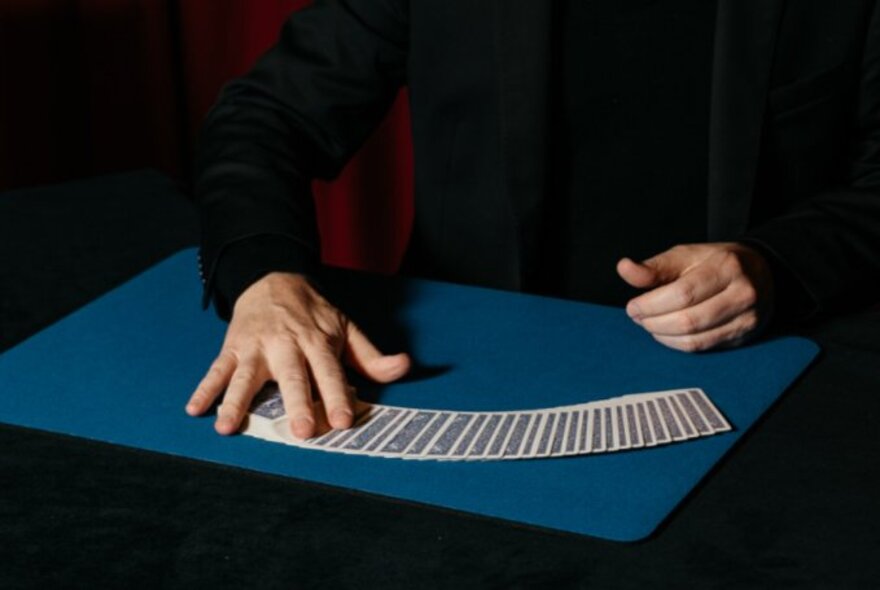 A magician's hands performing a card ribbon spread on a close-up mat.