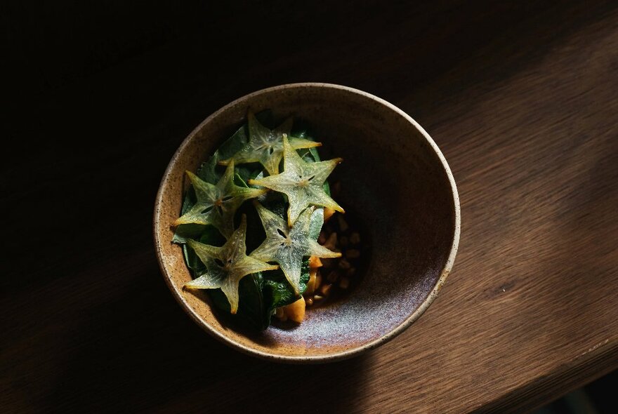 A pottery bowl on a wooden table, topped with sliced starfruit.