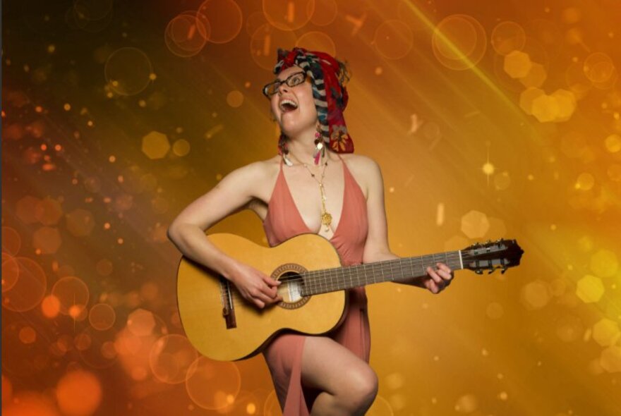 Musician with guitar playing against abstract golden background, mouth open and leg raised.