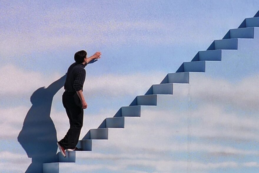 A still from the movie, The Truman Show, where Truman climbs a staircase in the sky-like wall of the movie set.