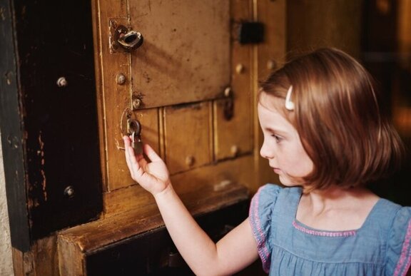 A young girl holding a padlock attached to an old cupboard.