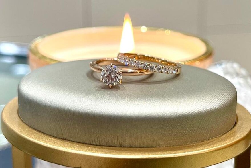 Two diamond rings resting on each other, a low candle flame in the background.