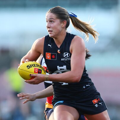 A Carlton AFLW player takes off with the football, ponytail flying out the back. 