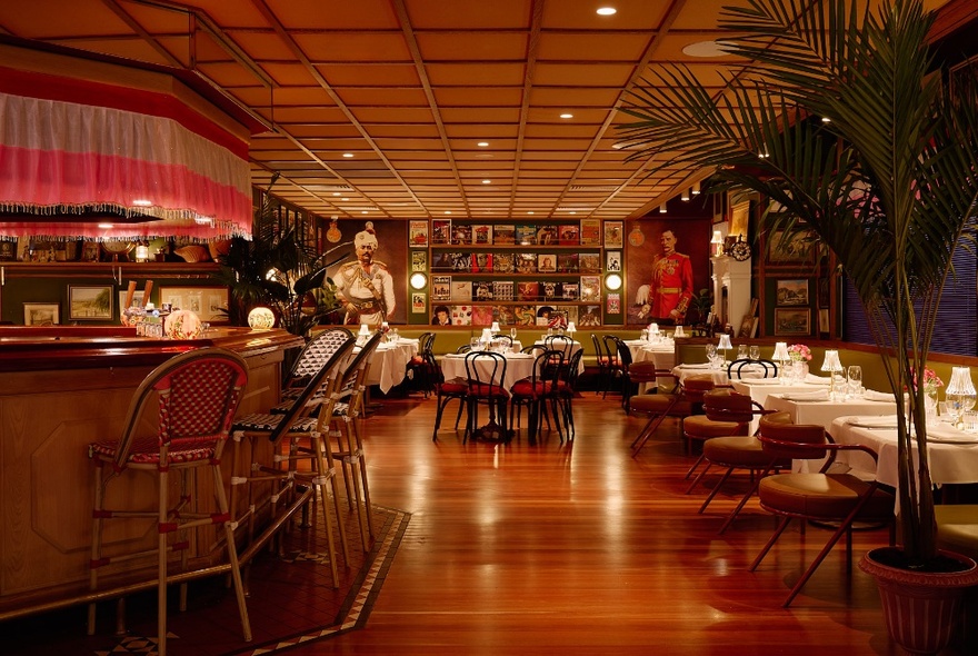 Interior of a pub with gleaming timber floors, a timber bar with barstools, and tables with white tablecloths.