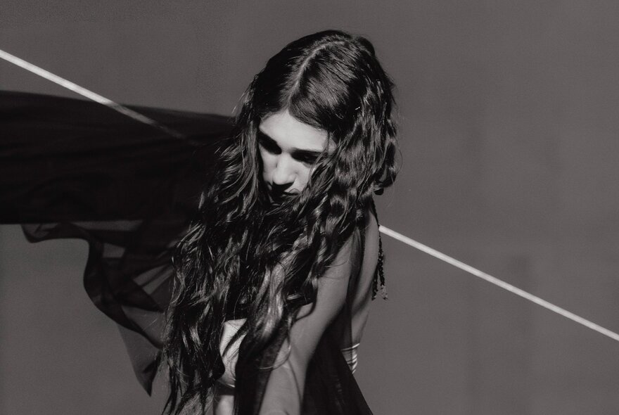 A dancer with long dark hair with a string or pole running through their back, across their shoulders. 