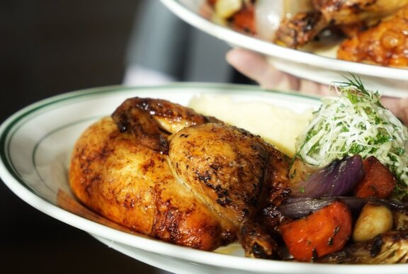 A close up of a roast chicken portion on a plate with slaw and roasted veggies.