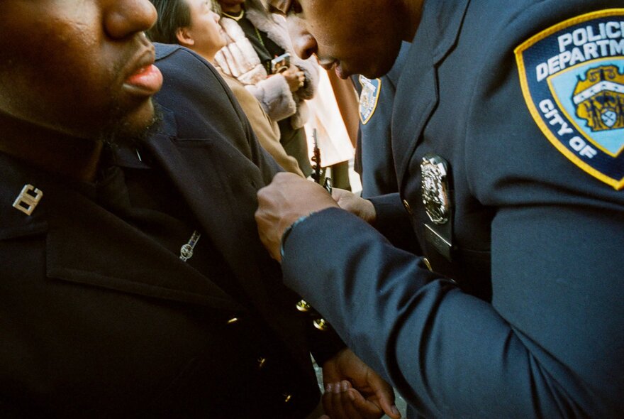 Close-up of an New York Police Department officer adjusting another officer's uniform, in a street setting.