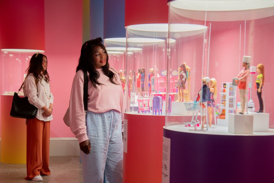 Two women explore a vibrant and colourful museum exhibition dedicated to Barbie.