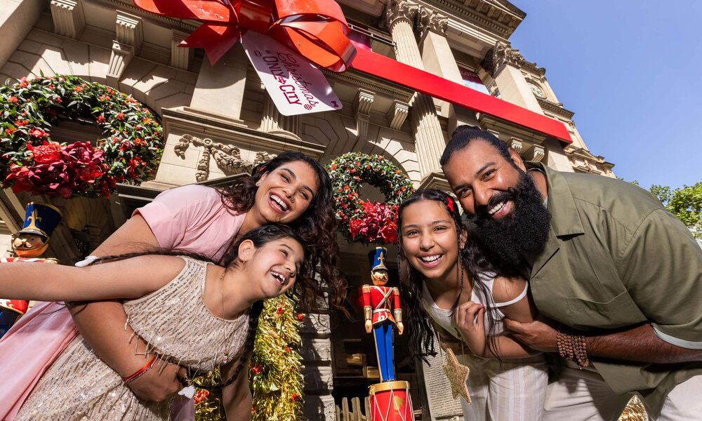 Family of four in front of Melbourne Town Hall that is decorated with Christmas decor.