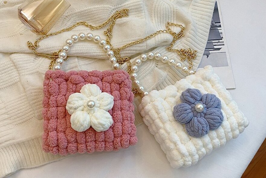 Two small knitted shoulder bags using plush soft fabric, with a flower detail and a chain strap, made in a cross-stitch workshop.