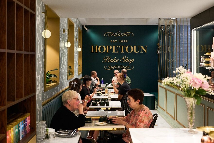 Customers seated at cafe tables in a room with mirror and plants.