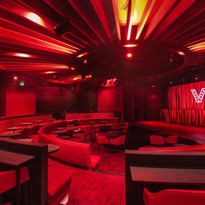 The red interior of the cabaret venue Viva, with a central stage surrounded by curved rows of seating, each with small tables nearby.