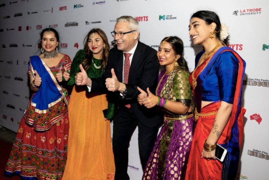 A group of smiling people on the red carpet at the Indian Film Festival Awards Night, posing for a photo with their thumbs up.