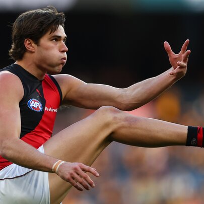 An Essendon Bombers AFL player with his leg in the air after kicking a football during a game.