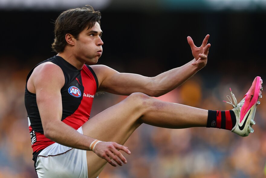 An Essendon Bombers AFL player with his leg in the air after kicking a football during a game.