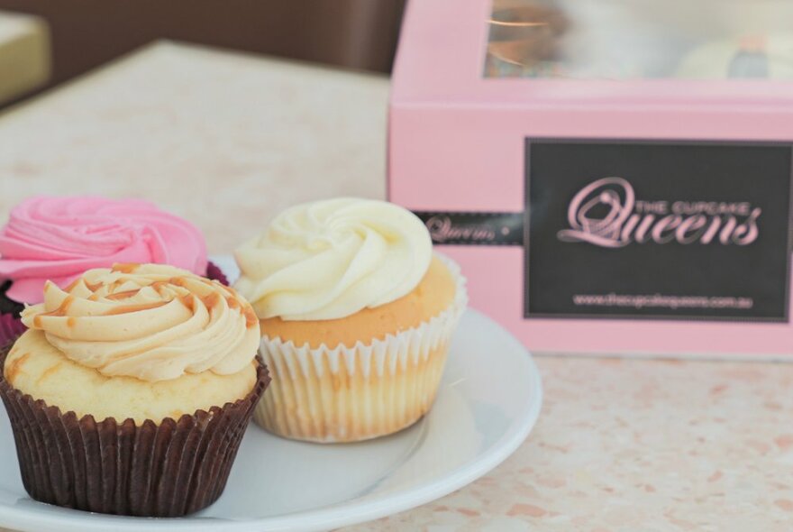 Three iced cupcakes on a plate next to a box of cupcakes. 