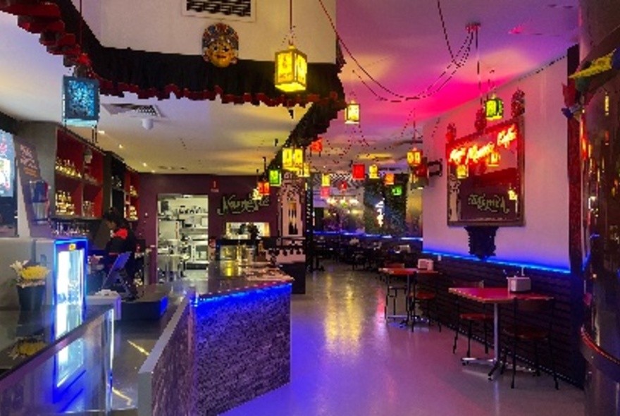 An empty cafe with a few tables and large long counter with dim coloured lights. 